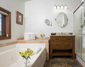 Wooden cabinet with a marble sink, to the right is a glass inclosed shower and to the left the jetted tub with Yellow flowers in a clear vase